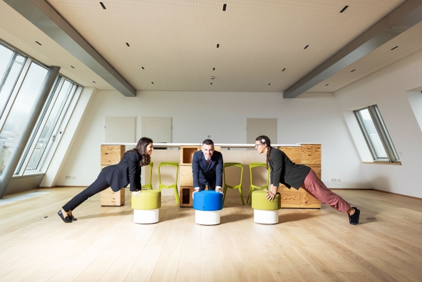 BTV Mitarbeiter*innen stützen sich auf bunten Hockern ab.