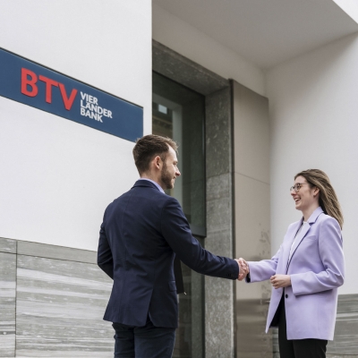 Ein Mann und eine Frau stehen vor einer Filiale der BTV Vier Länder Bank und geben sich die Hand. Das Firmenlogo ist im Hintergrund sichtbar.